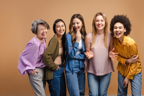 Five multi-ethnic women of different ages standing together laughing and showing genuine happiness and camaraderie