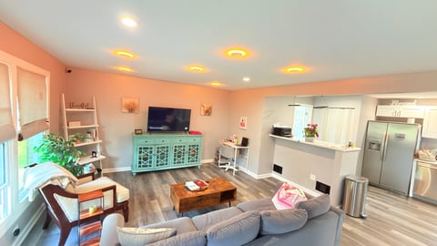 Modern living room with peach walls, gray sofa, wooden furniture, TV on green cabinet, and bright recessed lighting