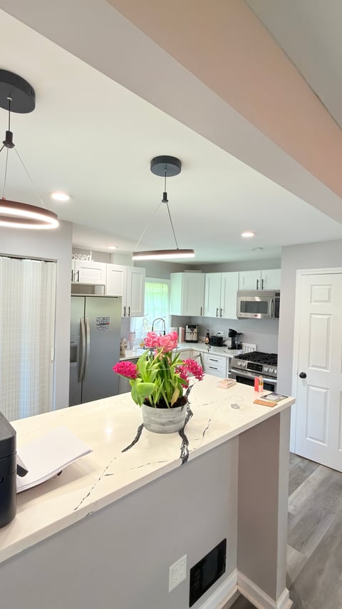 Modern kitchen with white cabinetry, marble island, pendant lights, and pink flowers in a vase on the countertop