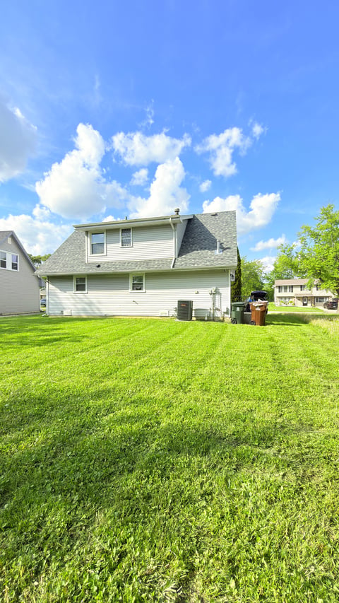 Two-story white suburban house with large green lawn and blue sky with white clouds